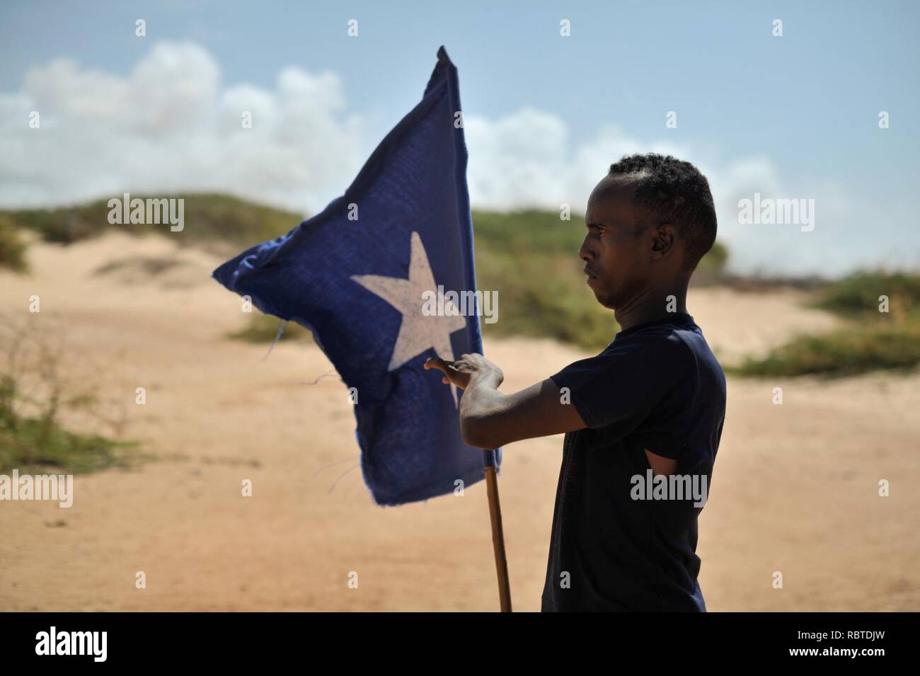 Un giovane uomo porta la bandiera somala mentre il leader di un gruppo di soldati durante una dimostrazione di una milizia locale, formata in modo da fornire la sicurezza nella città di Marka, Somalia, il 30 aprile. AU ONU (14081070785). Foto Stock