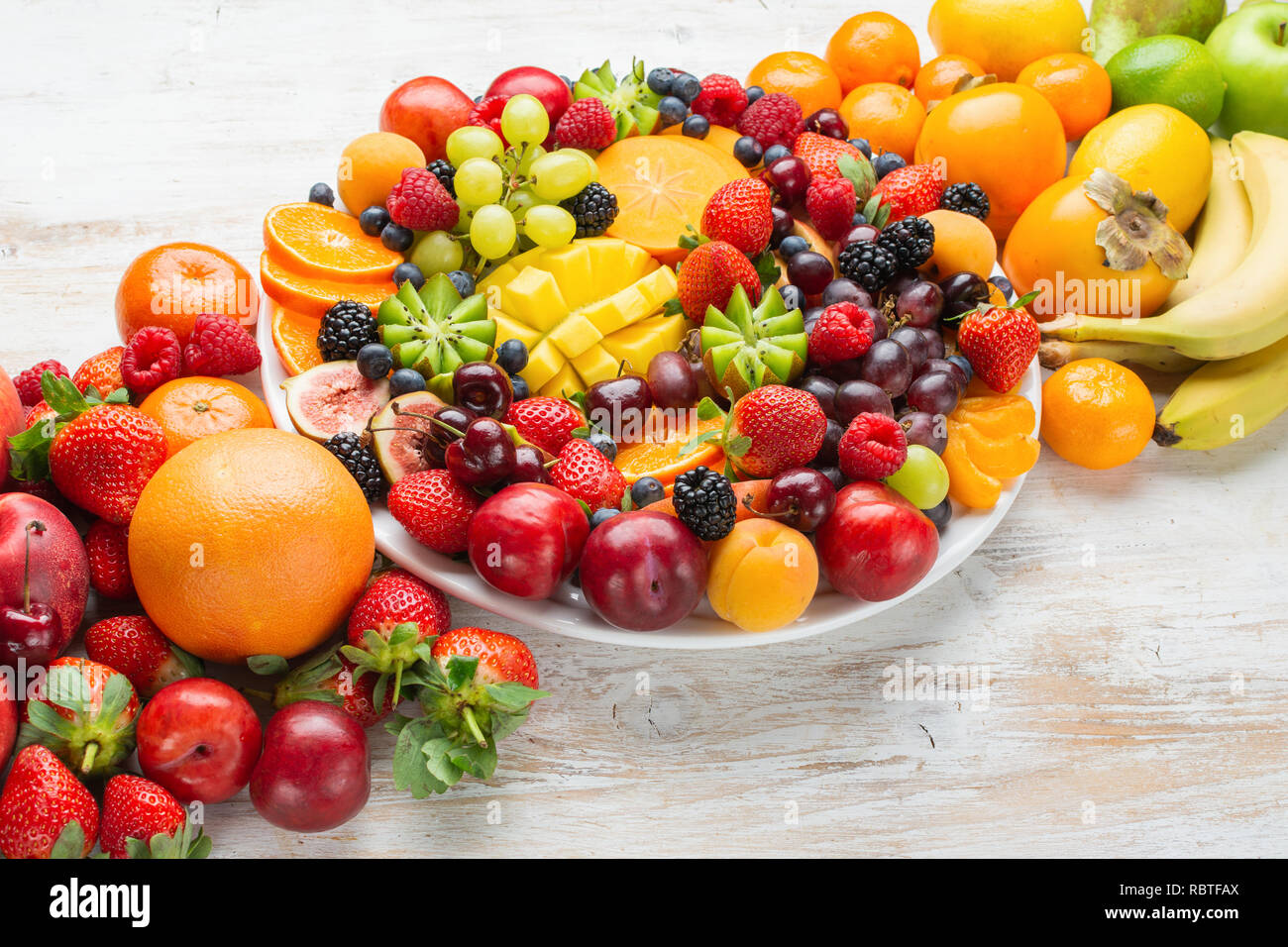 Piatto sano con colorati frutti arcobaleno, Fragole Lamponi arance Prugne Mele Kiwi uve mirtilli persimmon mango, spazio di copia Foto Stock