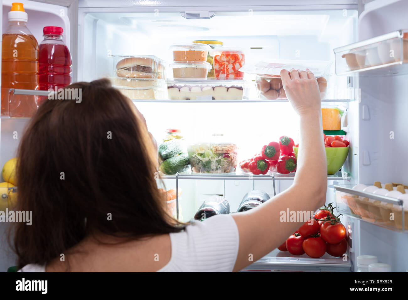 Vista posteriore di una giovane donna prendendo il cibo dal frigorifero Foto Stock