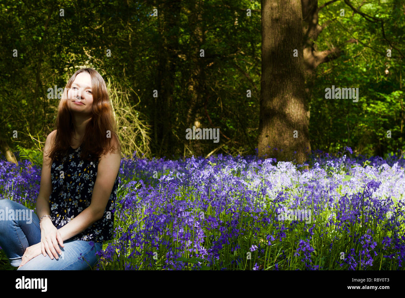 Le giovani donne, seduta in campo delle Bluebells vibranti Foto Stock