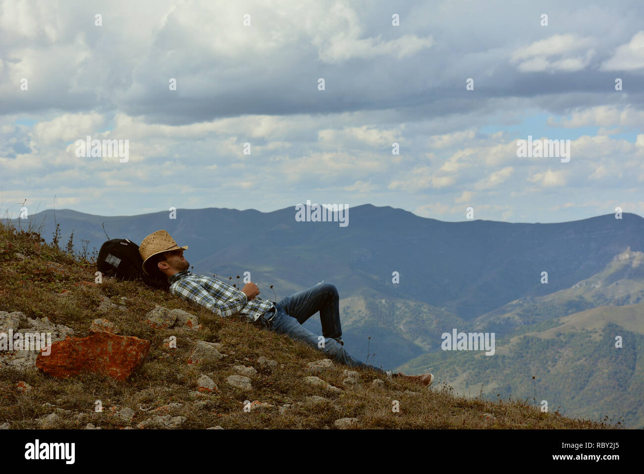 Giovane uomo in abiti da cowboy di riposo in montagna.Traveler godendo di una vista panoramica durante l'escursione, bello sfondo con paesaggio di montagna. Foto Stock