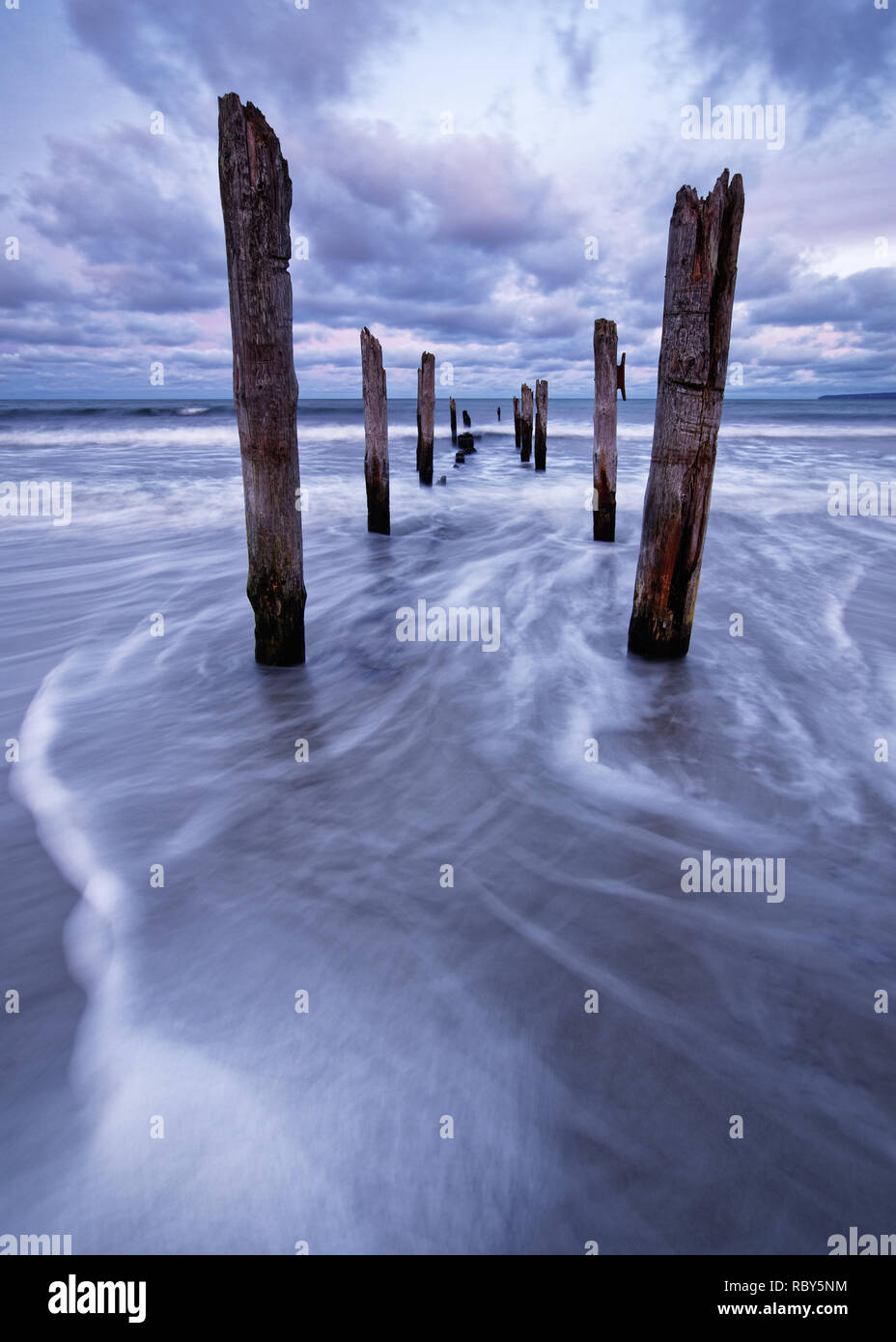 Vista panoramica di pali in legno su una spiaggia, il movimento delle onde è mostrato in aggiunta ad una colorata del cielo della sera - Location: Mar Baltico, Rügen Island Foto Stock