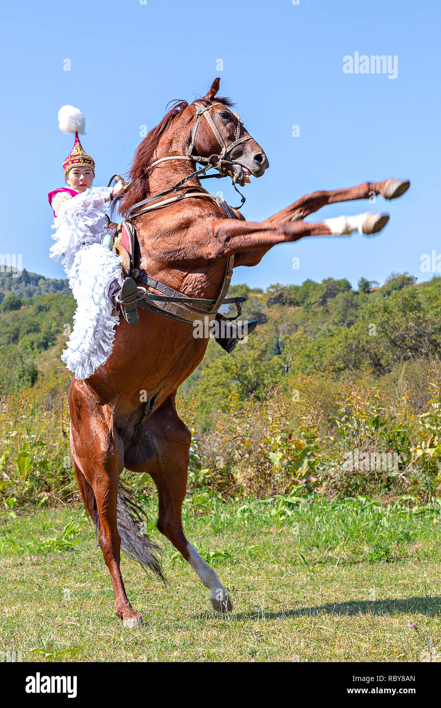 Il kazako donna in costume nazionale di allevamento fino il suo cavallo, ad Almaty in Kazakistan. Foto Stock