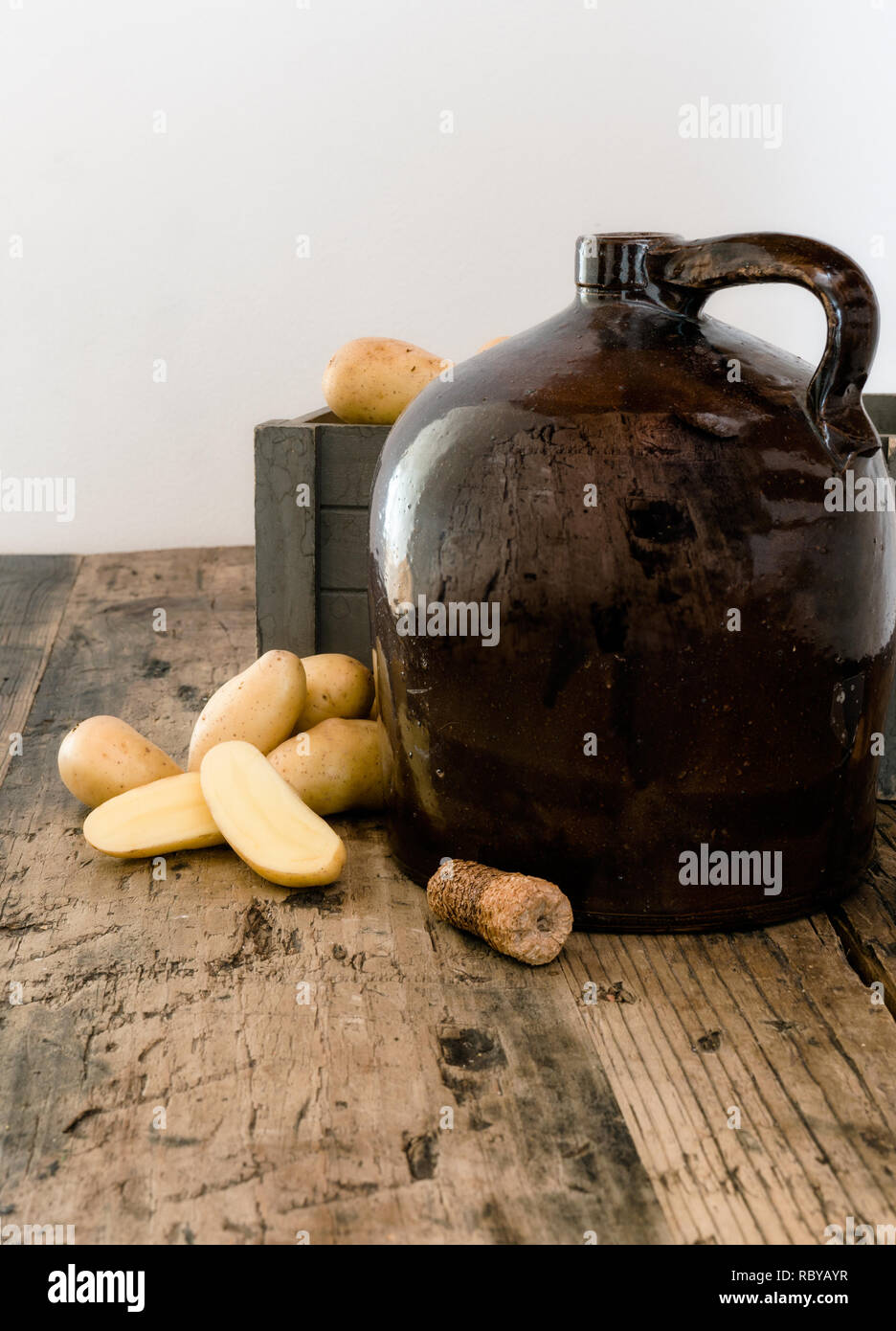Vintage moonshine brocca su una tavola in legno rustico con patate e pannocchia di sughero per la distillazione di liquori Foto Stock