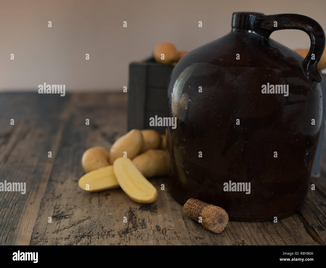 Vintage moonshine brocca su una tavola in legno rustico con patate e pannocchia di sughero per la distillazione di liquori Foto Stock
