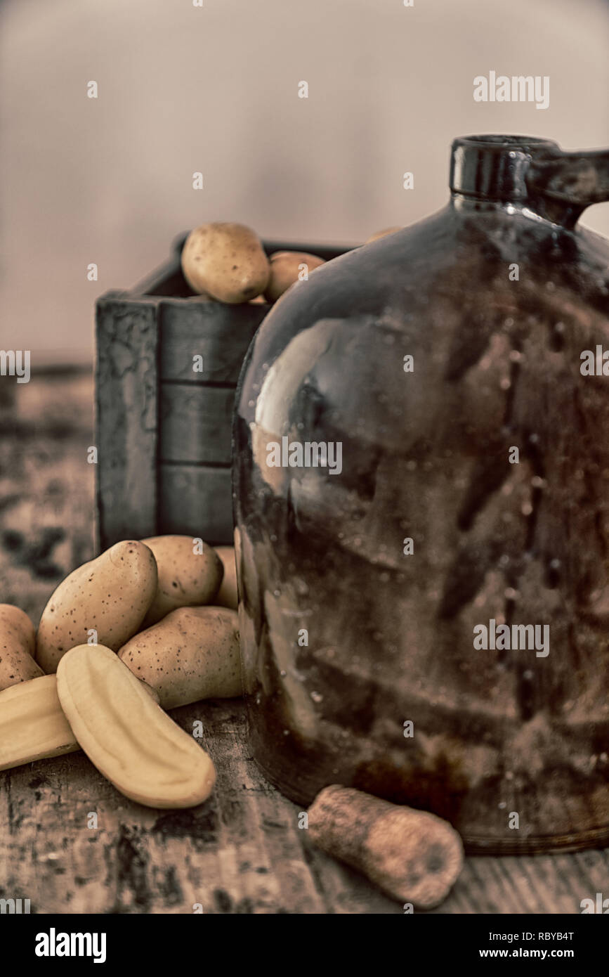 Vintage moonshine brocca su una tavola in legno rustico con patate e pannocchia di sughero per la distillazione di liquori Foto Stock