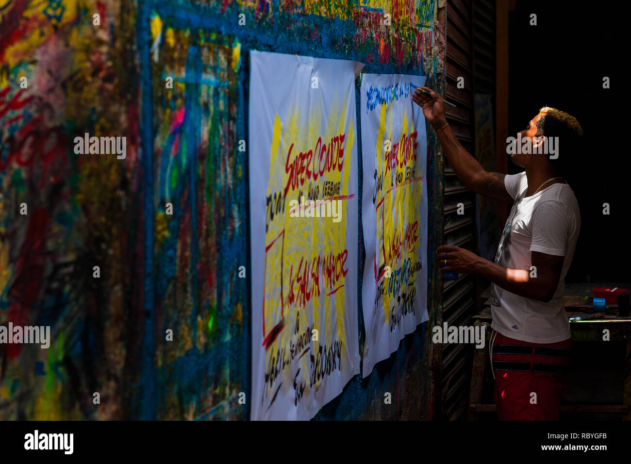 Un cartello colombiano pittore scrive con un pennello mentre si lavora sulla musica poster di partito nel segno atelier di pittura a Cartagena, Colombia. Foto Stock