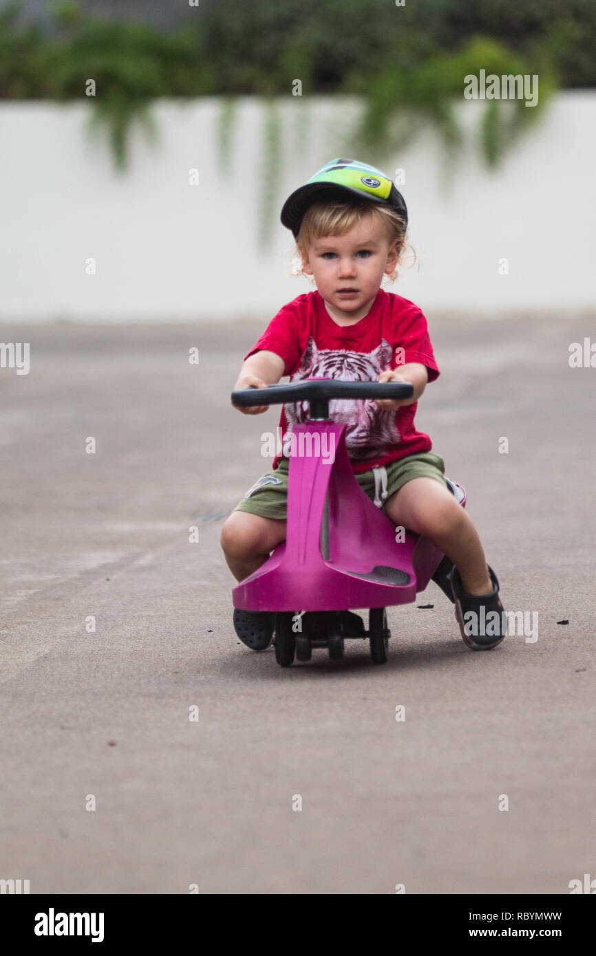 La foto di un capretto felice guida con un purple plasma auto come la corsa sul giocattolo Foto Stock