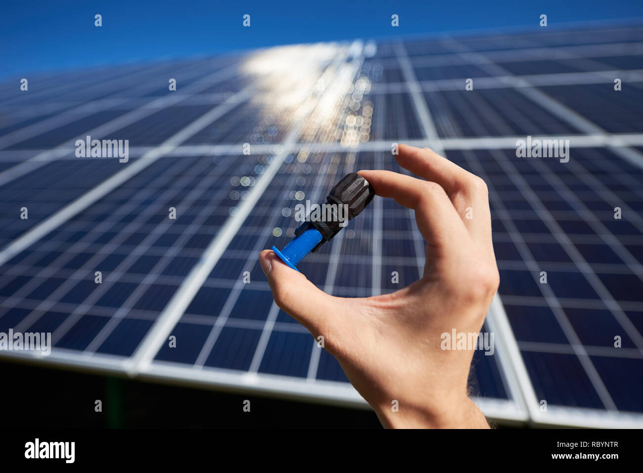 Mano d'uomo mantenendo piccolo dettaglio per la batteria solare installato nella parte anteriore del pannello solare sul background. Tendine su una superficie liscia. Innovativo high-tech Foto Stock