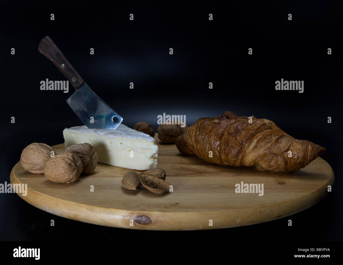 In legno piatto girevole con formaggio francese chiamato brie con la lama di un coltello e un croissant francesi e le noci e mandorle Foto Stock