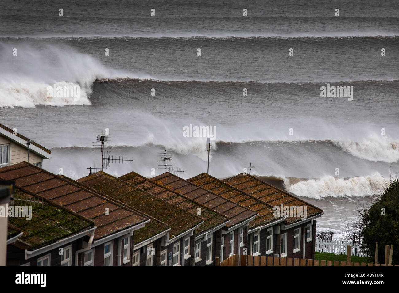 Venti Offshore pick up lo spruzzo da questi rulli Atlantico come essi vengono a riva di fronte all'antenna TV adornata chalets per le vacanze nella cittadina balneare di Foto Stock