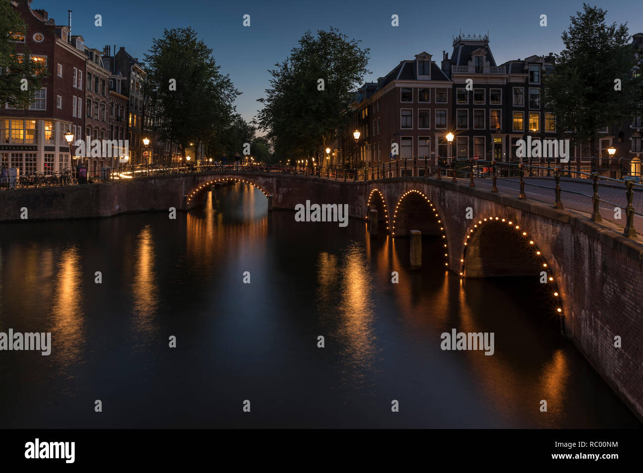 Canale di Amsterdam e il bridge al tramonto. Il canale è calma e le luci intorno i ponti arcate sono riflettendo sull'acqua liscia. Foto Stock