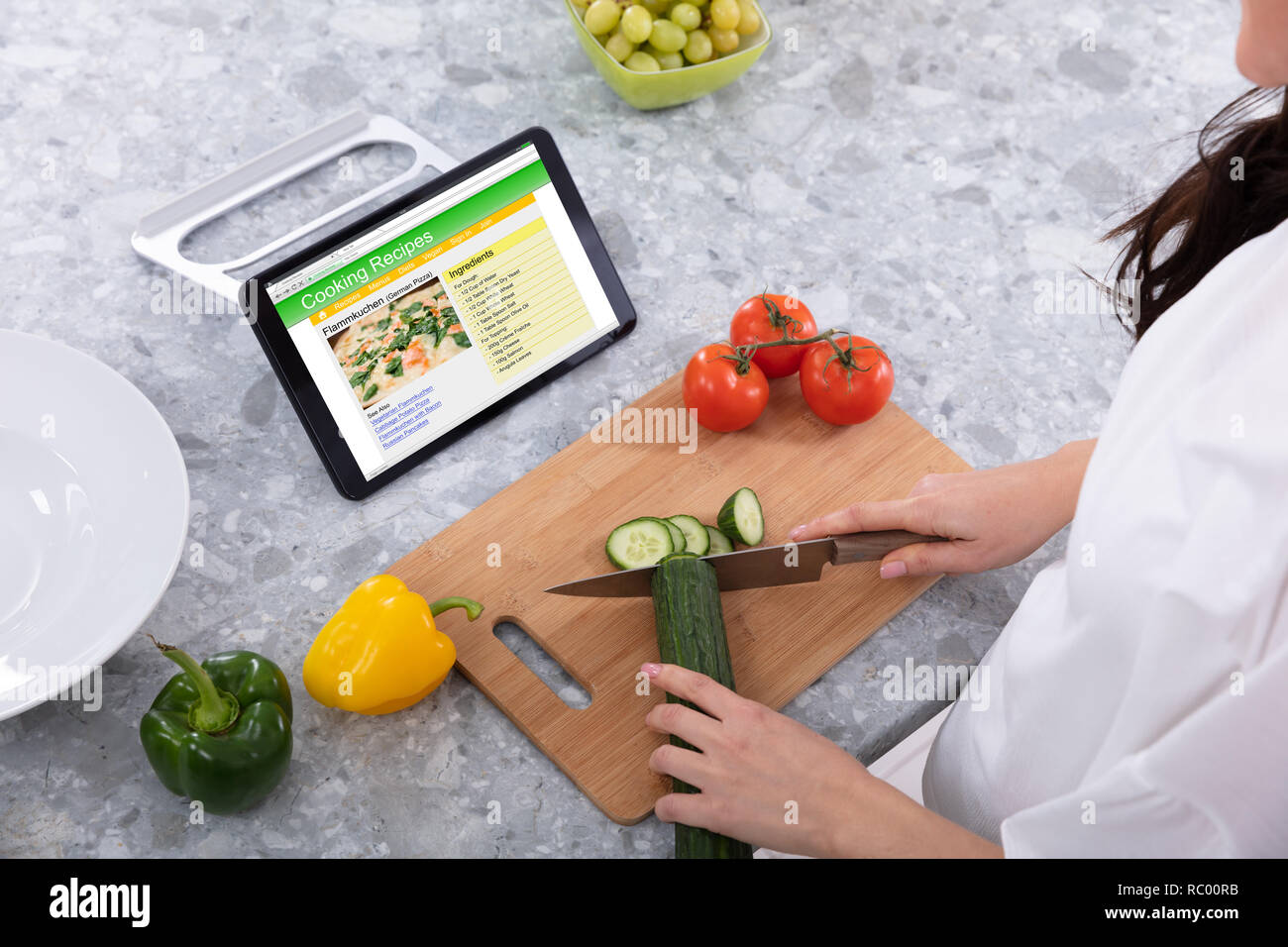 Donna cetriolo di taglio con il coltello da cucina vicino a ricette di cucina sulla tavoletta digitale schermo Foto Stock