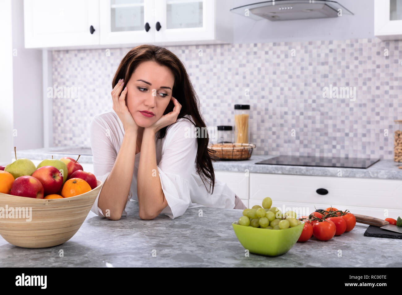 Frutta fresca di fronte sconvolto giovane donna appoggiata sul banco di cucina Foto Stock