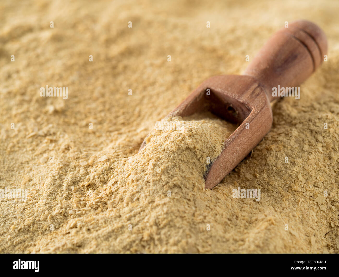 Il lievito nutrizionale dello sfondo. Nutrizionali di lievito inattivo con un piccolo cucchiaio di legno. Copia dello spazio. Il lievito nutrizionale è vegetariano super con sapore di formaggio, per una sana alimentazione Foto Stock