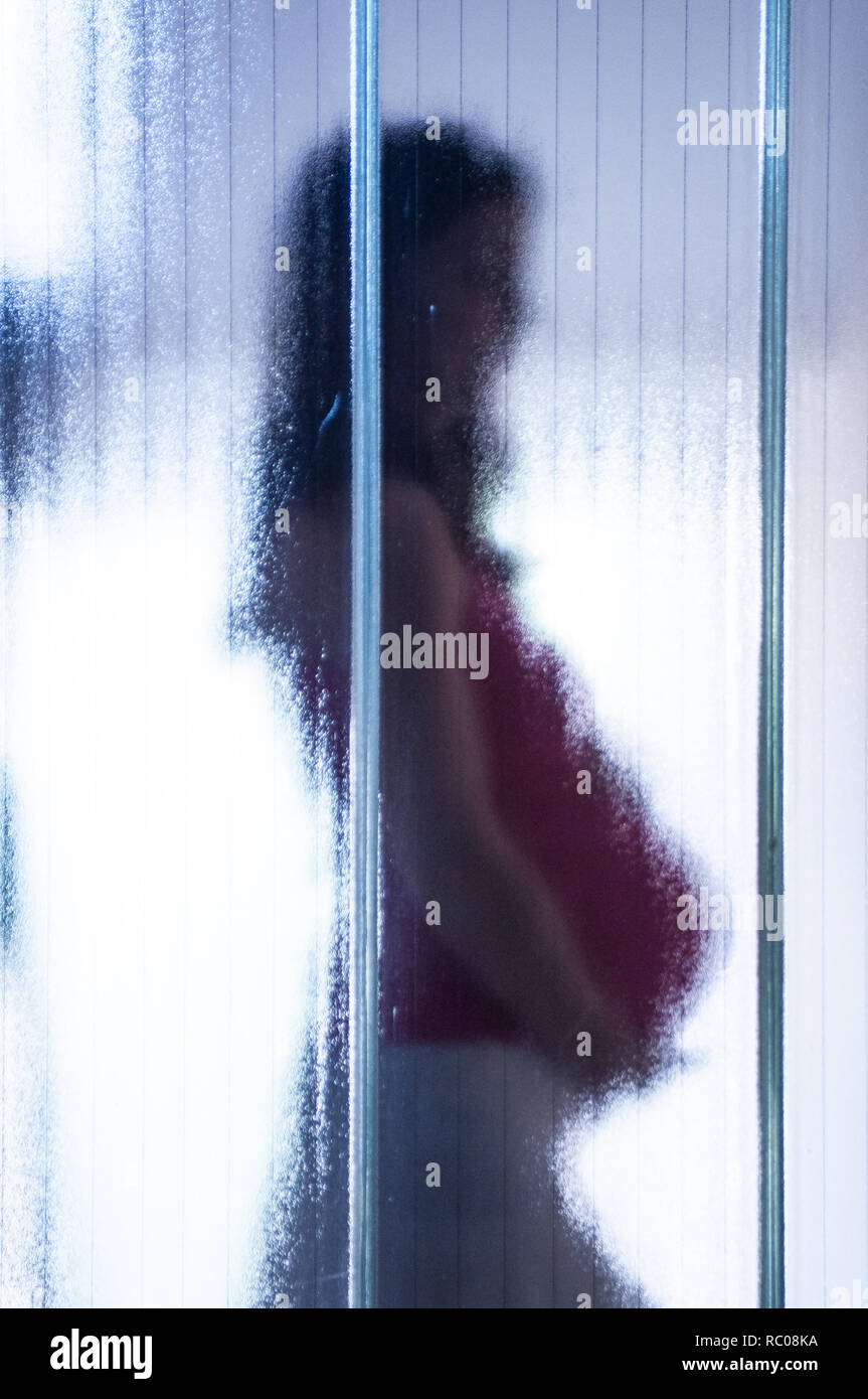 Giovane donna incinta dietro il vetro opaco con dark moody atmosfera, simbolo del post partum depressione Foto Stock