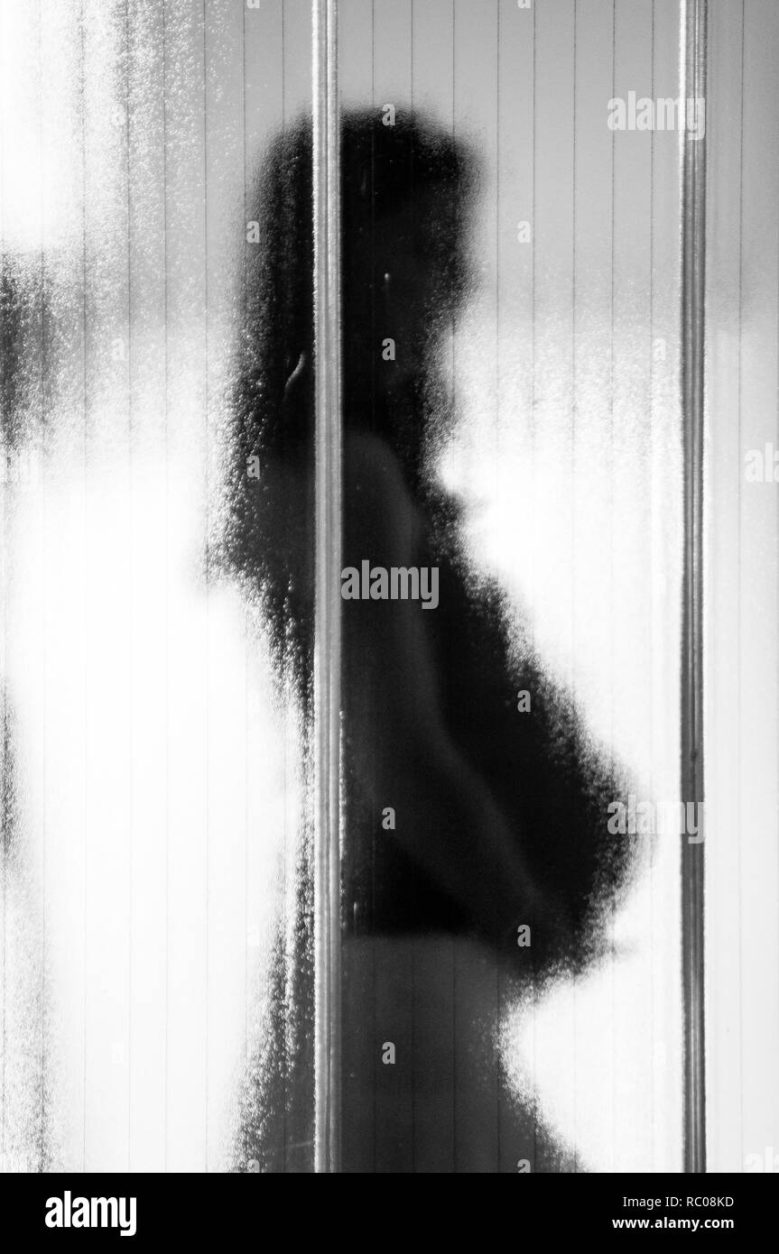 Giovane donna incinta dietro il vetro opaco con dark moody atmosfera, simbolo del post partum depressione Foto Stock