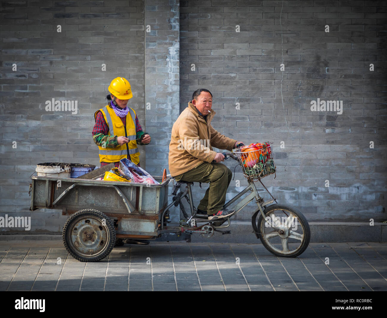 Uomo che trasportano materiale di lavoro su un triciclo nel centro di Pechino, Cina Foto Stock