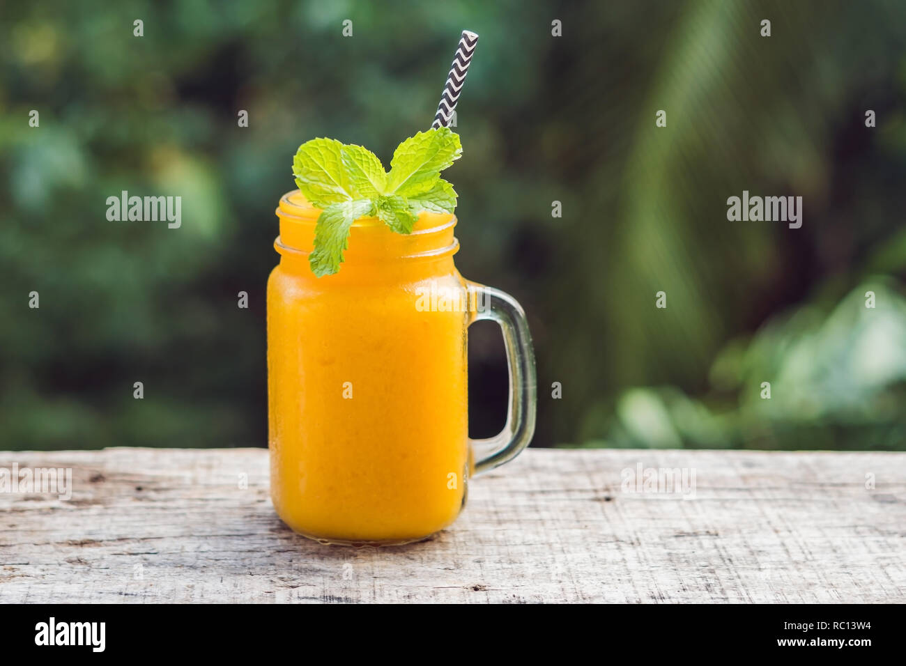 Frullato di mango in un vetro Mason jar e mango su uno sfondo verde. Mango agitare. La frutta tropicale concept Foto Stock