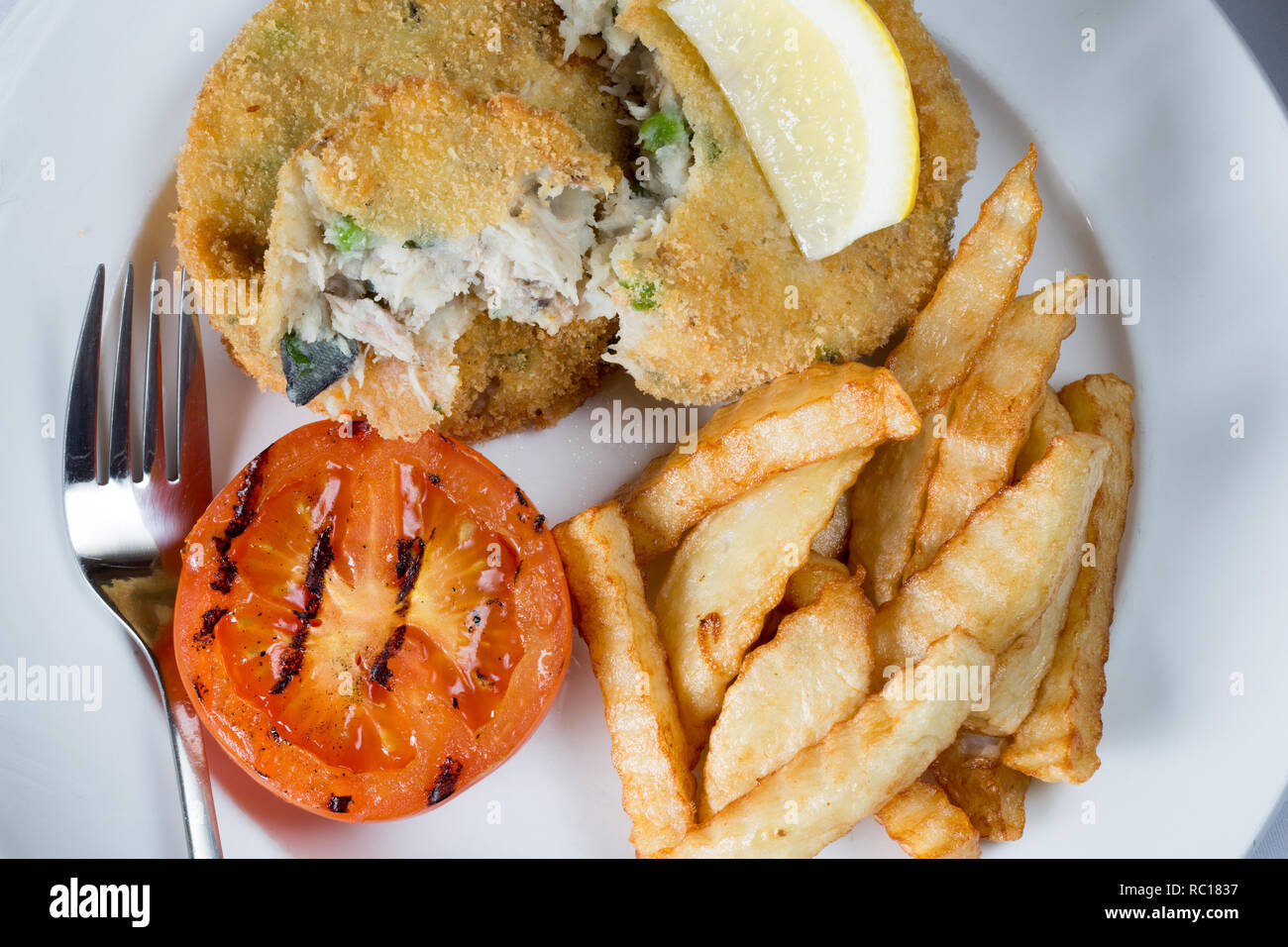 Placcato in un pranzo leggero in casa di sgombro e il segnale di PEA fishcakes con patatine/patatine fritte e grigliate di pomodoro e di limone fresco guarnire a cuneo. Foto Stock