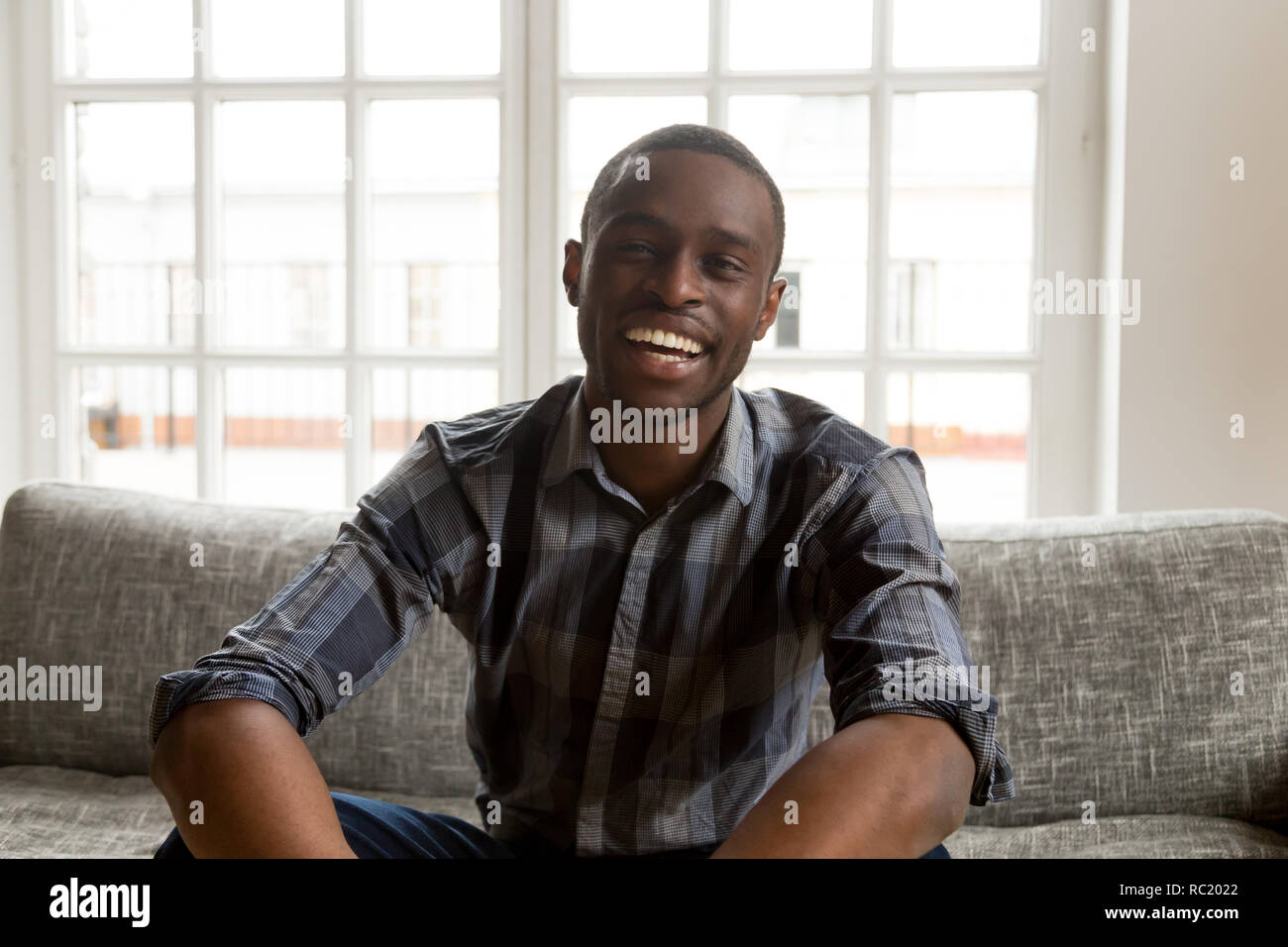 Sorridente maschio africano vlogger guardando la telecamera seduta sul lettino Foto Stock