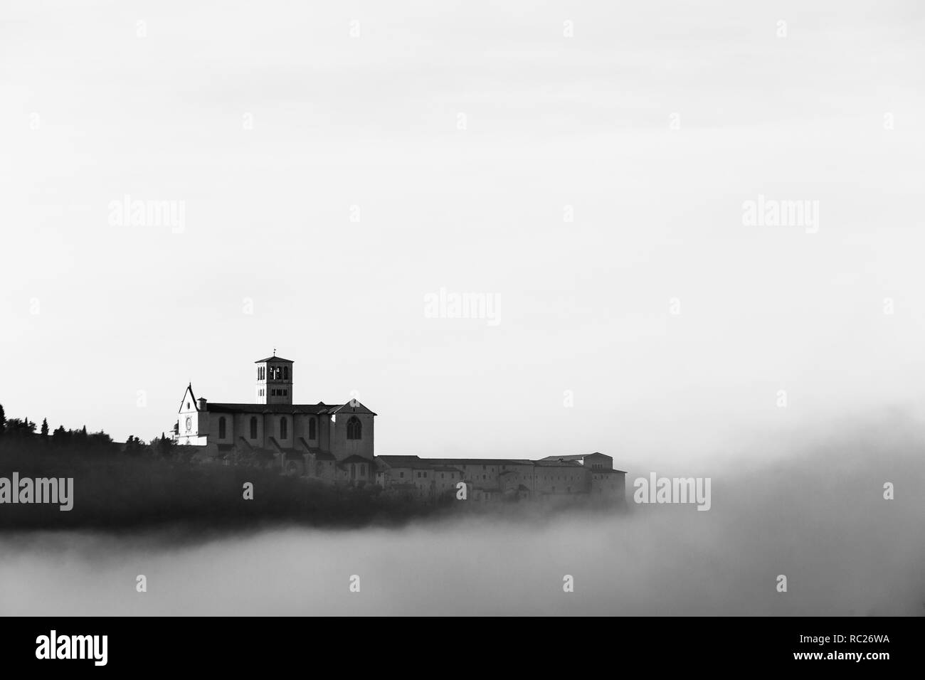 Una vista della Basilica di San Francesco in Assisi nel mezzo della nebbia sotto un cielo profondo con le nuvole Foto Stock