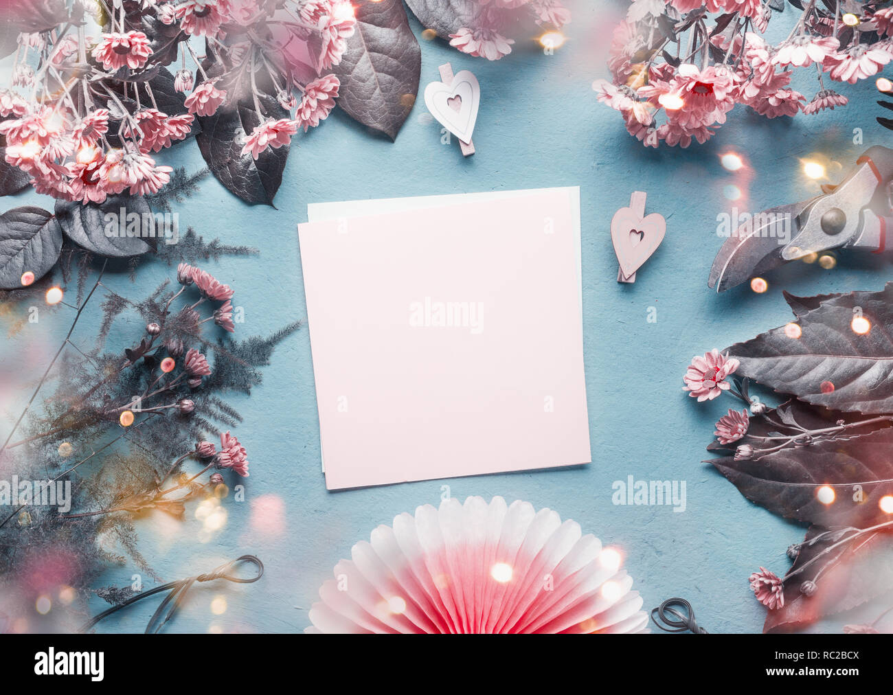 Bigliettino vuoto su blu fioraio scrivania con fiori di colore rosa, cuori e carta origami ventola. Abstract il concetto di saluto. La festa della mamma, compleanno mock up. Co Foto Stock