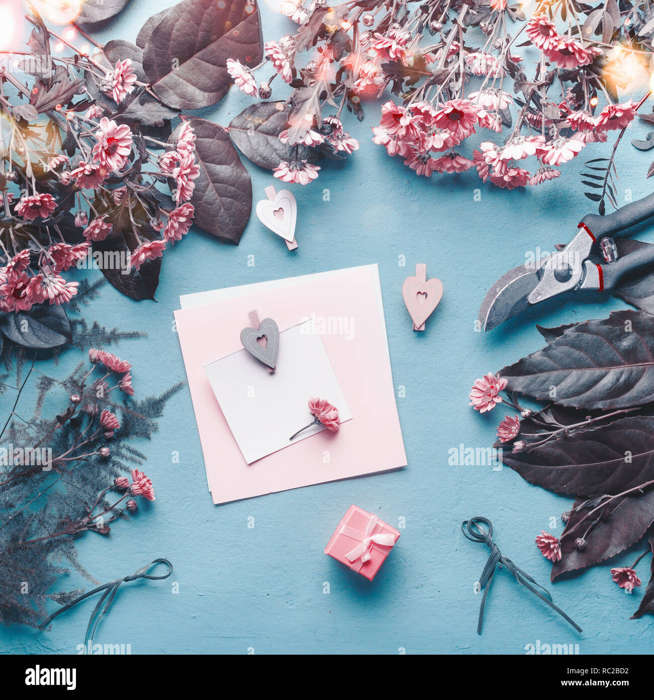 Bigliettino vuoto su blu fioraio scrivania con fiori di colore rosa, cuori e confezione regalo. Abstract il concetto di saluto. La festa della mamma, compleanno mock up. Copia dello spazio. Foto Stock