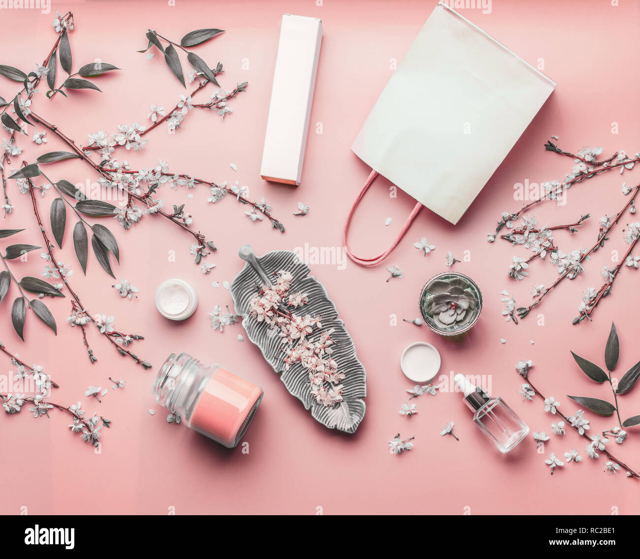 Concetto di cosmetici. Vari prodotti per il viso e la carta shopping bag su rosa pastello con sfondo di fiori di ciliegio e foglie, vista dall'alto il telaio. Spazio di copia Foto Stock