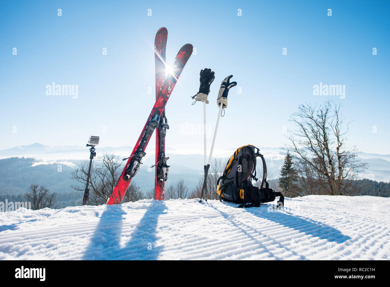 Le attrezzature da sci - sci, zaino, bastoncini, guanti e azione fotocamera su monopiede, sulla parte superiore della pista da sci a ski resort in montagna Foto Stock