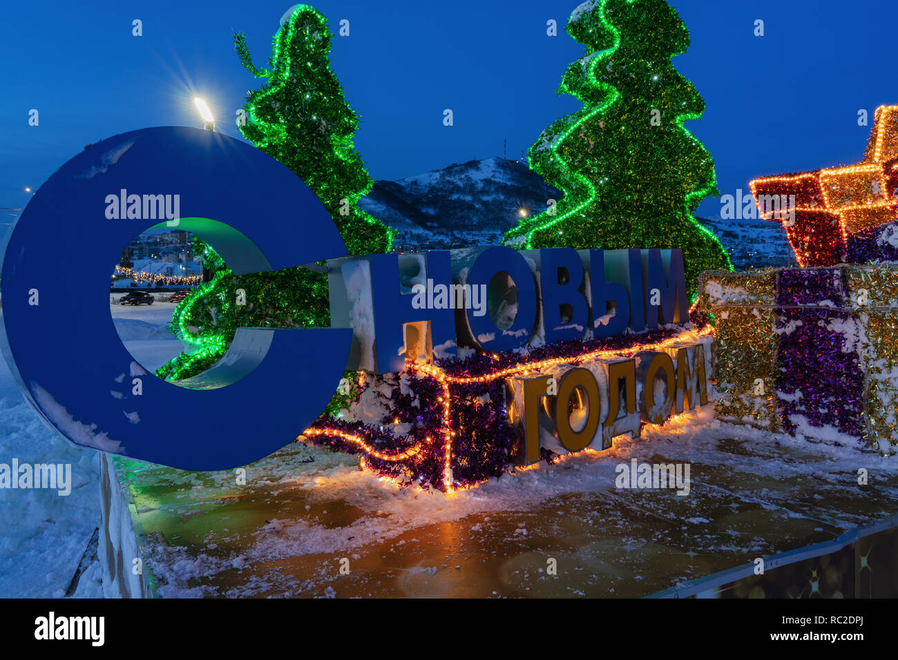 Vista notturna illuminata di composizione di festa con una iscrizione in russo felice anno nuovo in città nevoso Foto Stock