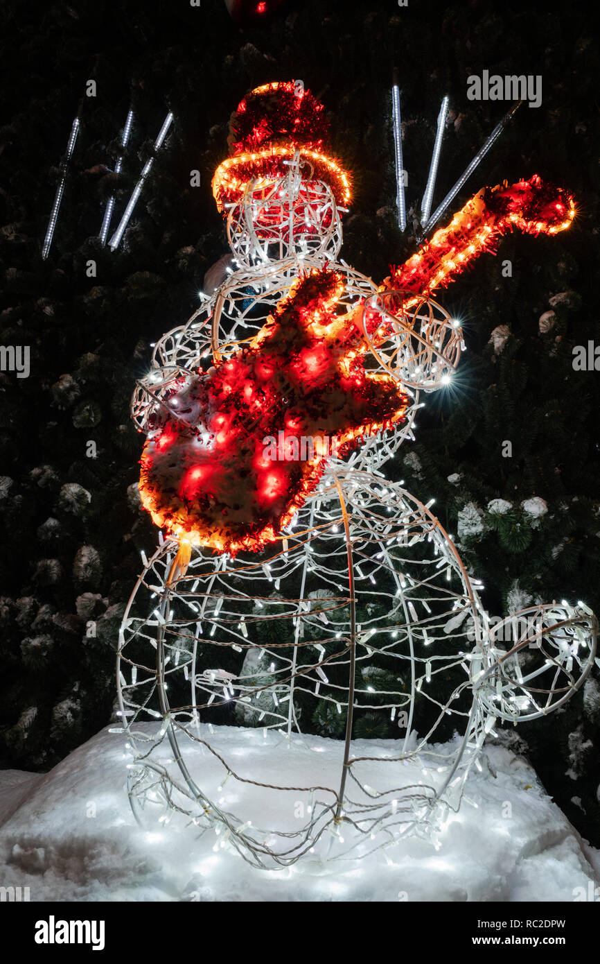 Pupazzo di neve chitarrista da ghirlande luminose con la chitarra rossa e top hat sorge su sfondo dell albero di Natale Foto Stock