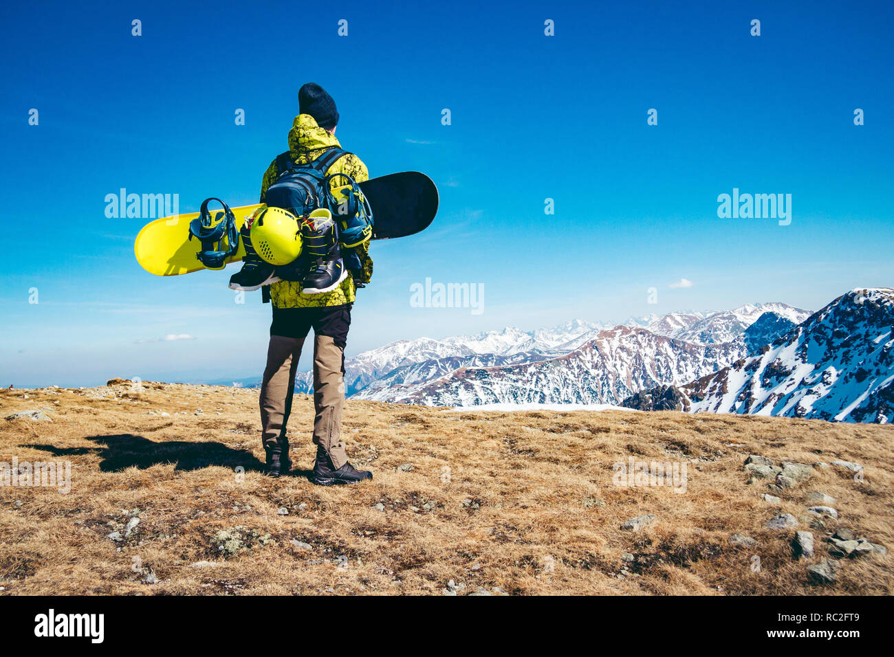 Un uomo in piedi sulla cima di una montagna con lo snowboard gear strapped al suo zaino Foto Stock