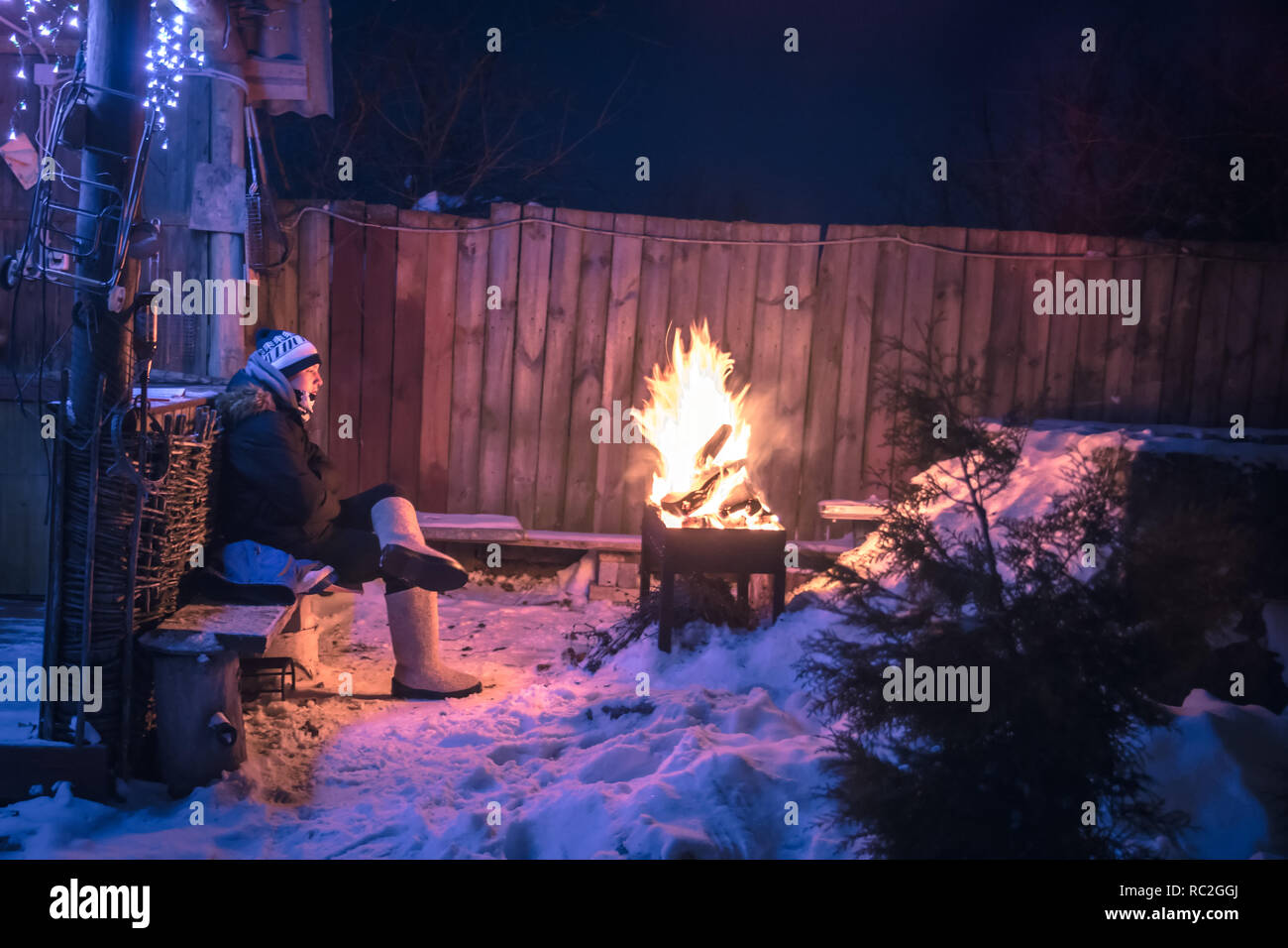 Inverno riflessivo adolescente lonely boys mancante e ottengo caldo a fuoco nella notte paesaggio innevato Foto Stock