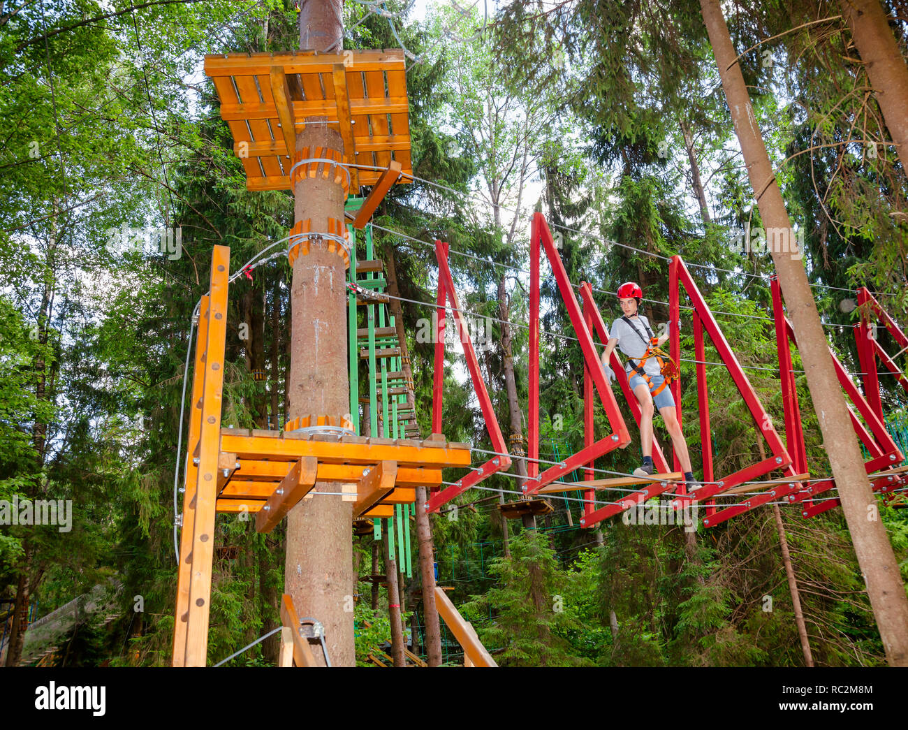 Ragazzo adolescente passando appeso ponte di corde ostacolo a un corso di funi in outdoor parco avventura Foto Stock