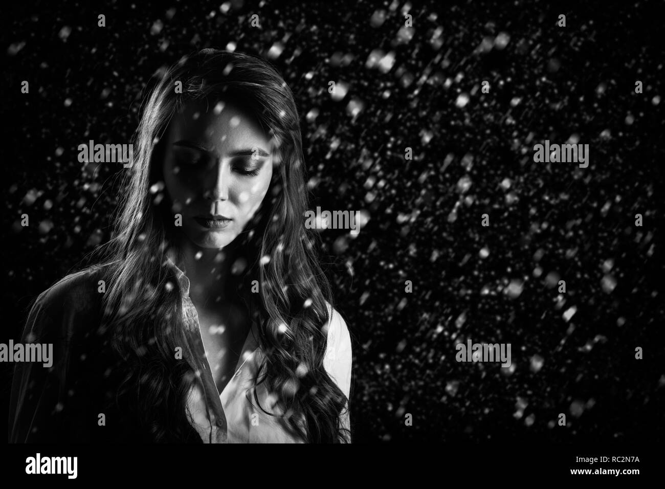 Triste pensieroso donna sulla camicia bianca su sfondo nero con spazio copia guardando verso il basso sotto la caduta di neve monocromatico Foto Stock
