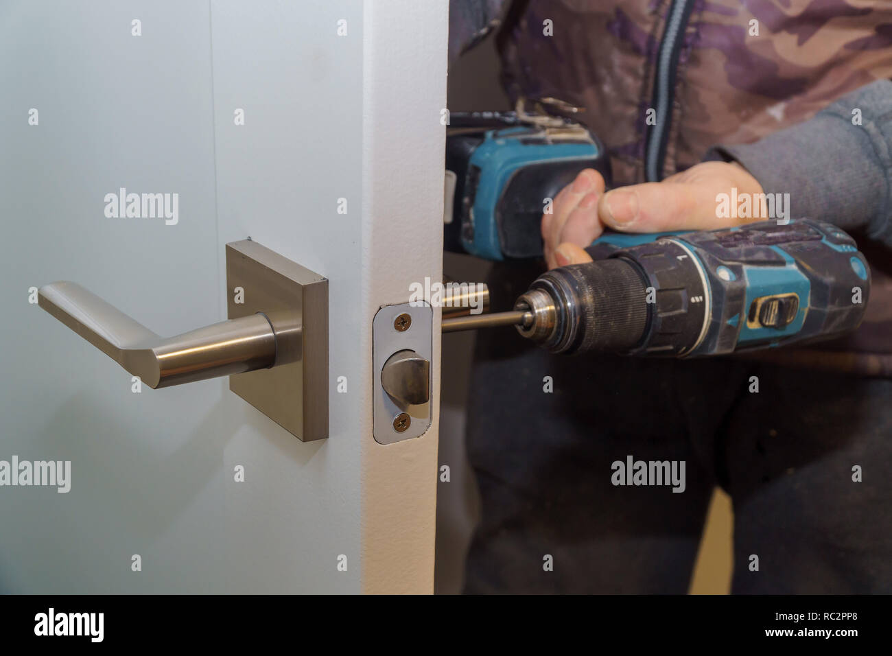 Installare la maniglia della porta con una serratura, falegname serrare la vite utilizzando un trapano elettrico cacciavite, close-up. Foto Stock