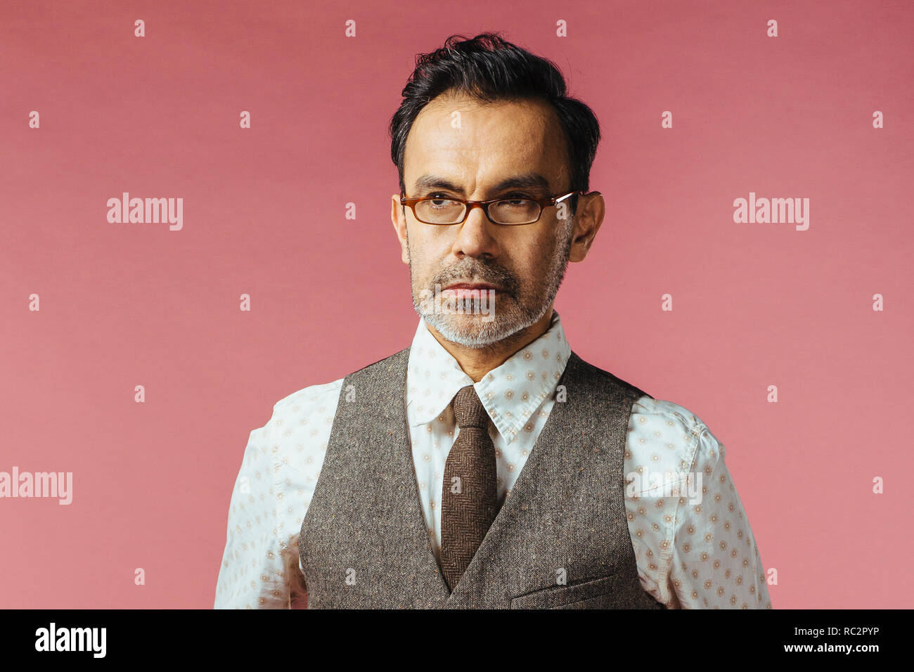 Ritratto di un uomo maturo in gilet e bicchieri, isolato in rosa Foto Stock