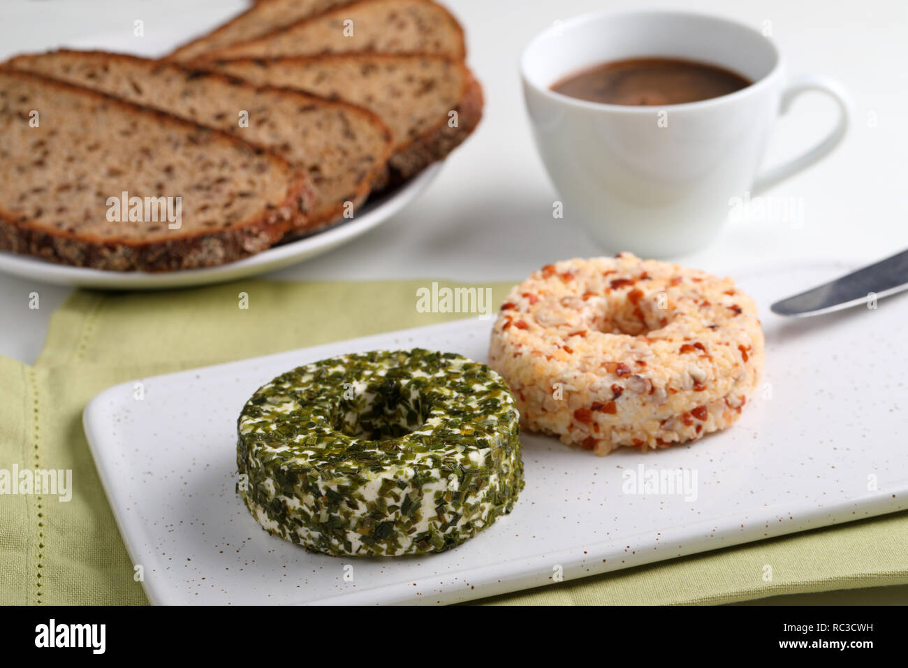 Turni di formaggi lettone con verdi, dadi e pepe su una ceramica tagliere per la prima colazione con caffè Foto Stock