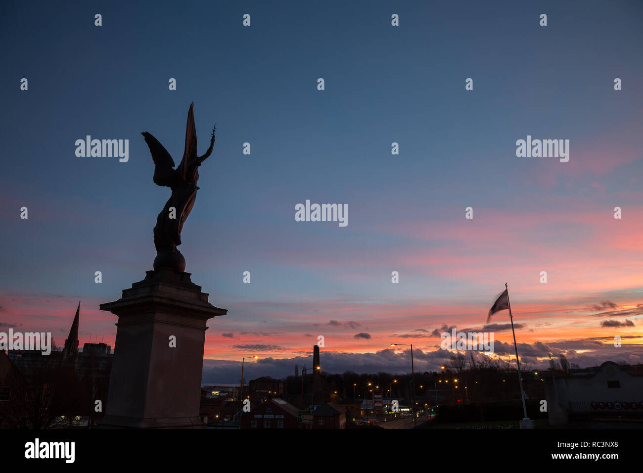 Kidderminster, Regno Unito. Il 13 gennaio, 2019. Regno Unito: meteo il sole tramonta a Kidderminster dopo un insolitamente calda giornata con temperature che raggiungono i 10 gradi celsius. La scultura di un angelo di pace può essere visto qui retroilluminati da il tramonto colorato al di fuori di St Mary's Church, Kidderminster. Credito: Lee Hudson/Alamy Live News Foto Stock