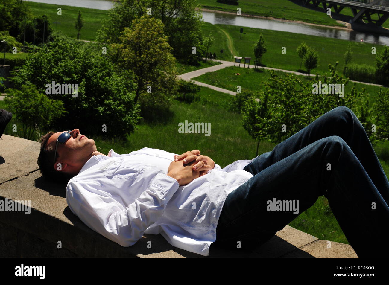 Uomo con una camicia bianca e occhiali da sole si trova sulla parete a Dresda e gode della vista sulla valle dell'Elba. Foto Stock