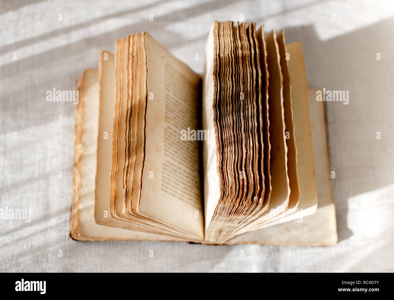 Aprire il vecchio libro con diffusione pagine sbiadite, visto da vicino da sopra il tavolo rustico con tovaglia bianca Foto Stock