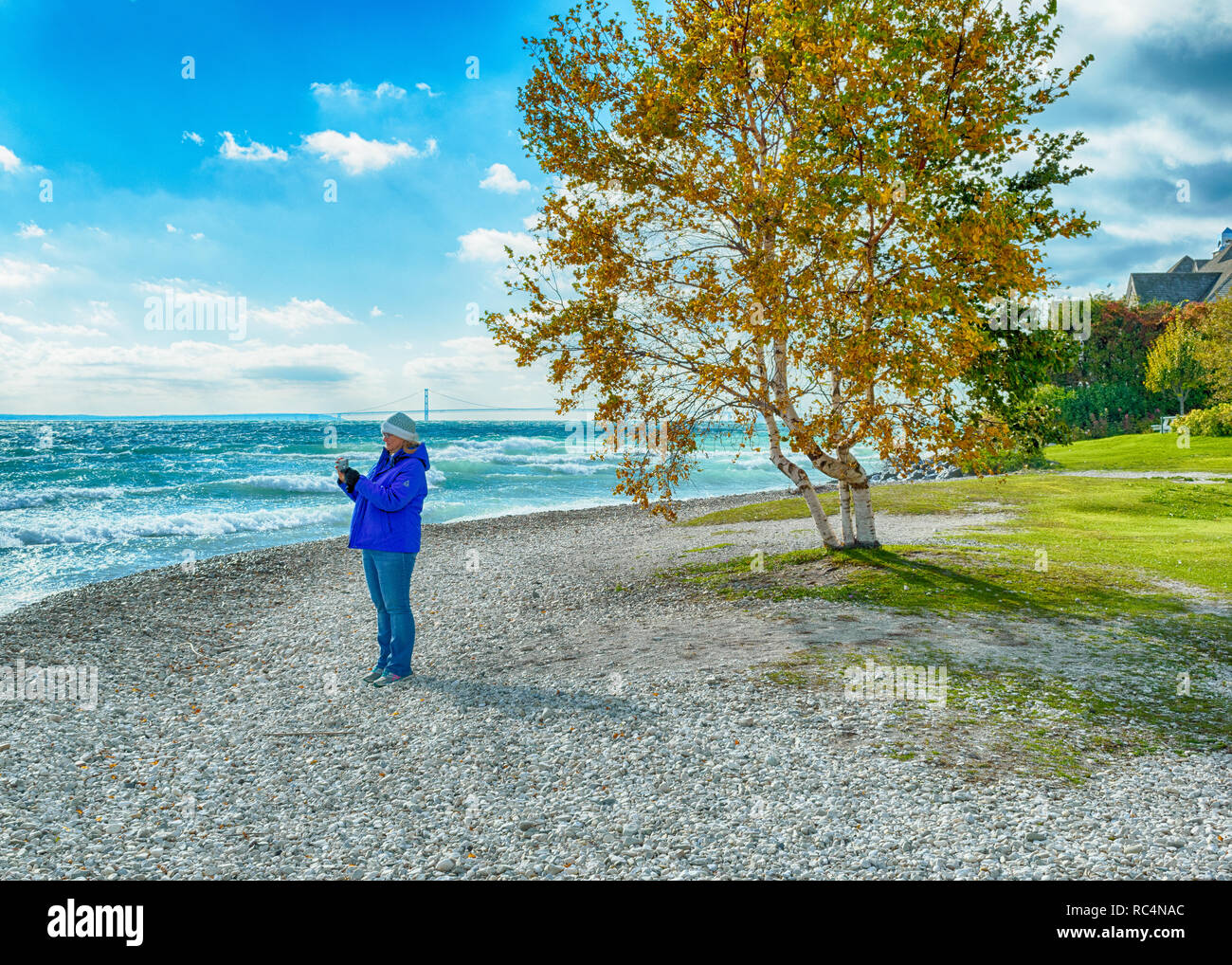 Donna in piedi sulla spiaggia sassosa sull isola di Mackinac prendendo foto di onde Foto Stock