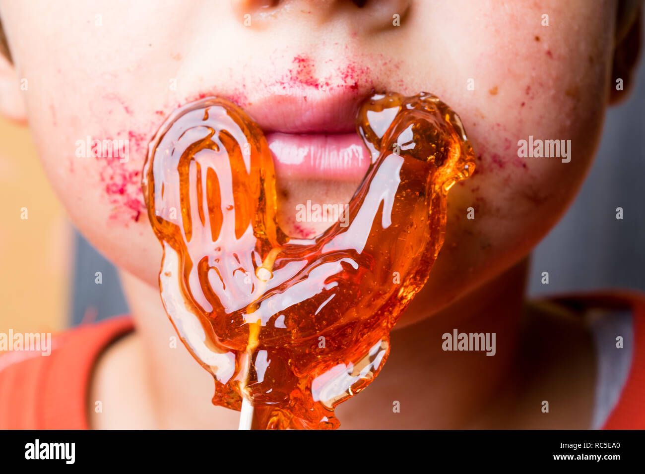 Ragazzo succhia lecca-lecca, baby mangia rosso-arancione chupa-chups,  bocca, labbra rosa, candy in mano, metà ragazzo del viso Foto stock - Alamy