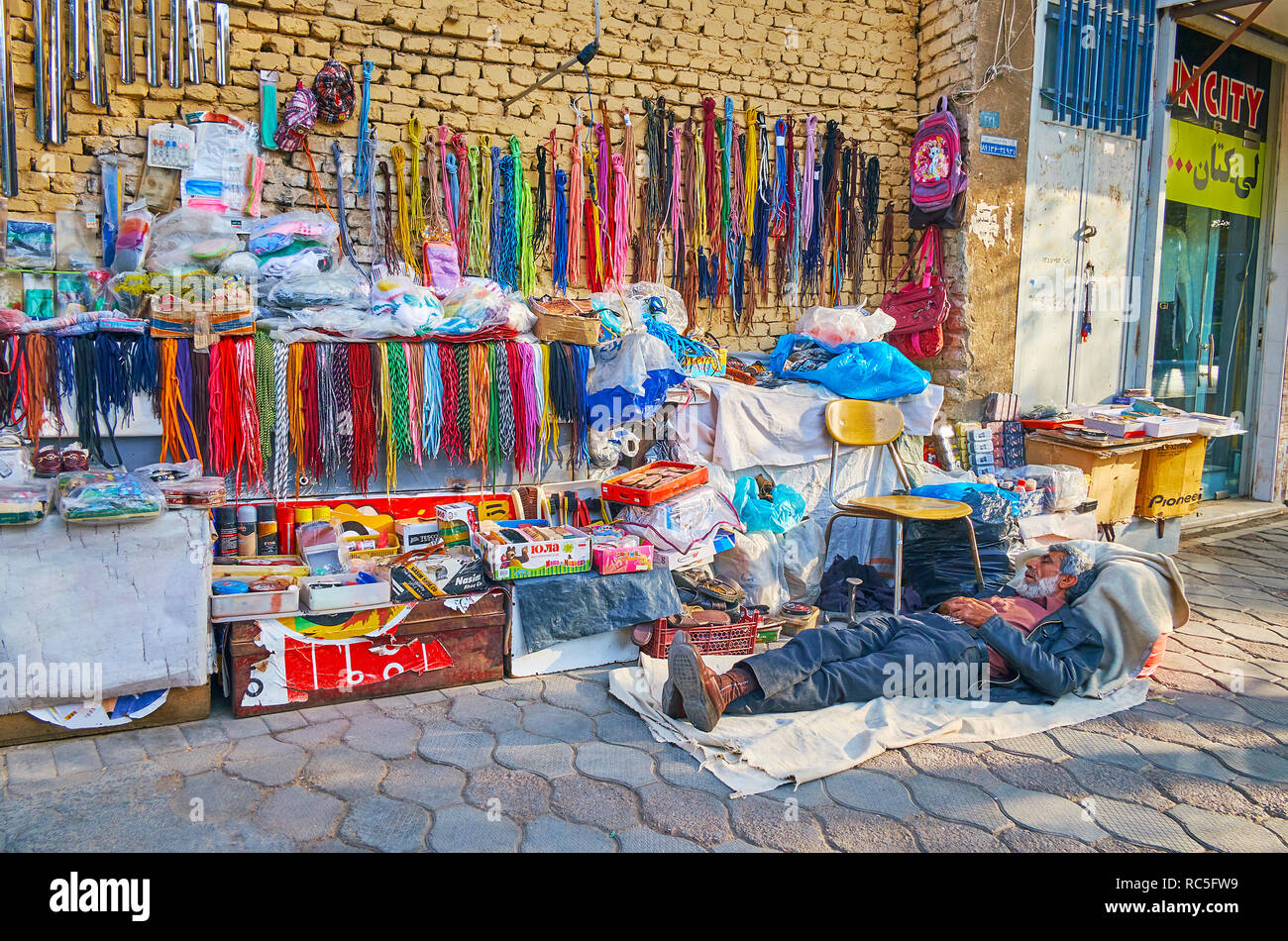 YAZD, IRAN - 18 ottobre 2017: gli anziani merchant dorme sul pavimento durante la siesta pomeridiana al suo piccolo stallo esterna della calzatura prodotti per la cura di un Foto Stock