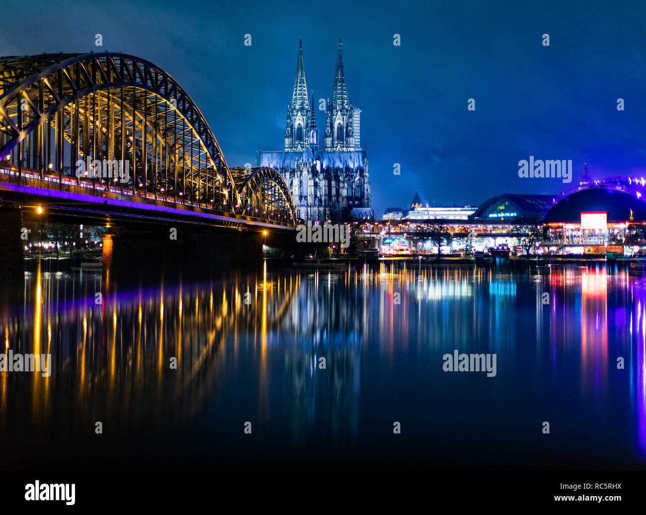 Die Hohenzollernbrücke (l), der Köllner Dom (m) und der Musical Dome (r) spiegeln sich bei blauer Stunde in Regenwasser auf einer Mauer. Foto Stock