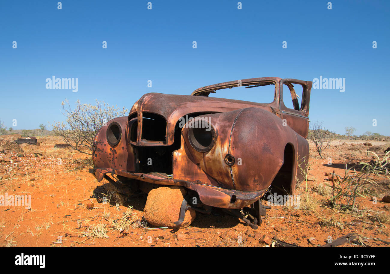 Un arrugginito vecchia auto giace devastata e abbandonata nell'Outback australiano con il blu del cielo e terra rossa. Foto Stock