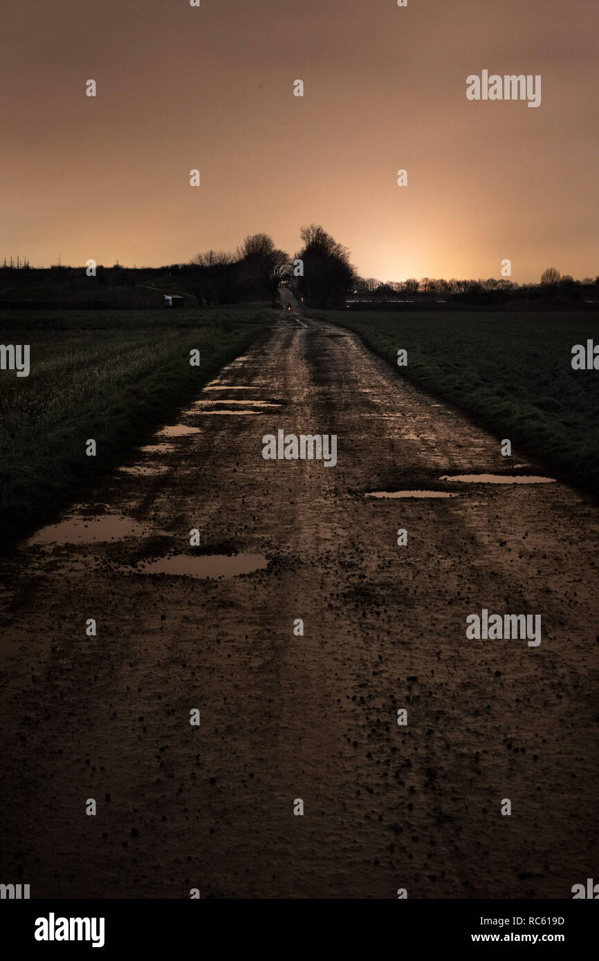 Un bagnato su strada sterrata con buche dopo il tramonto. Foto Stock