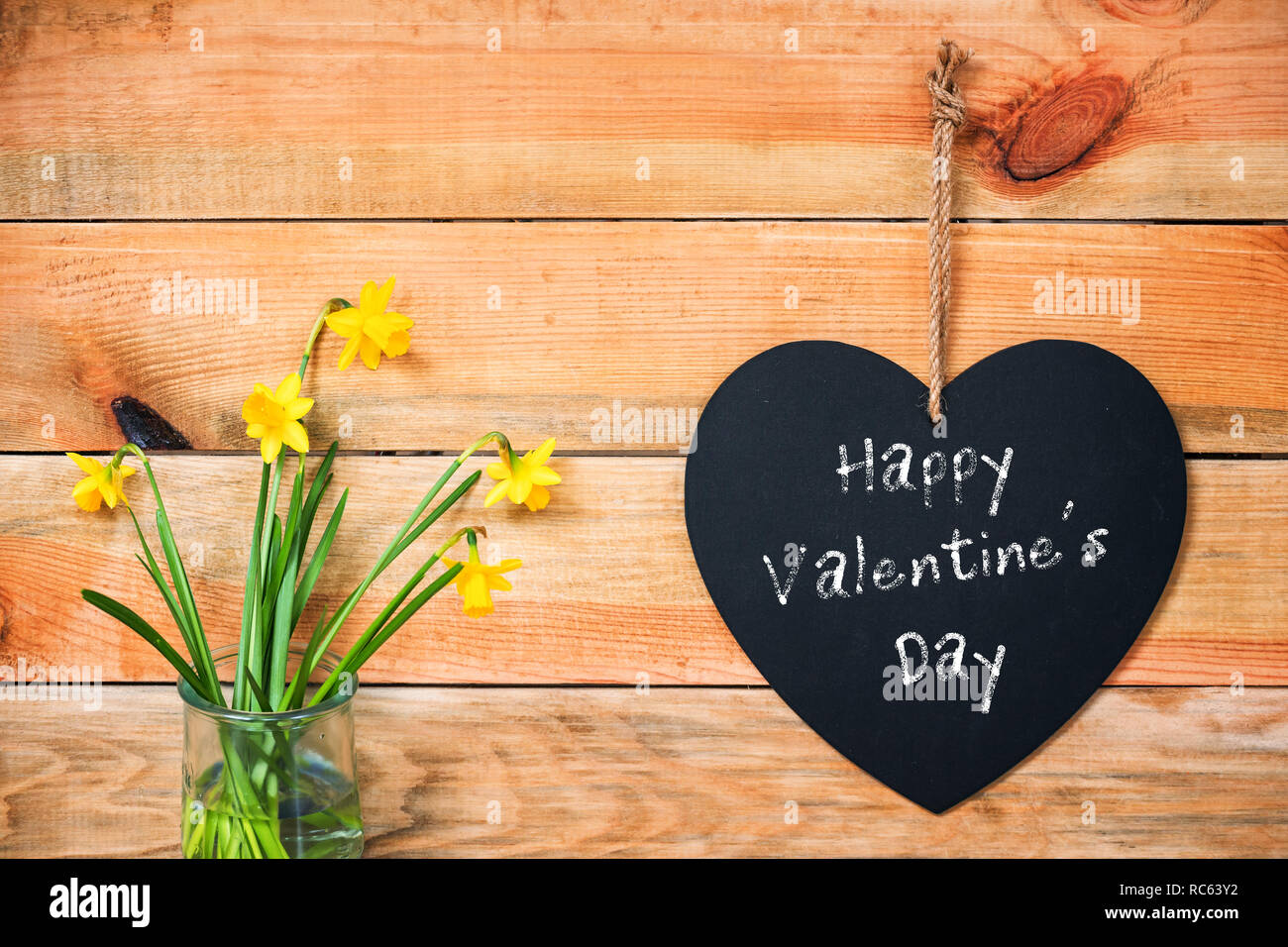 Buon San Valentino Scritto su una lavagna a forma di cuore, narcisi e tavole di legno sfondo Foto Stock