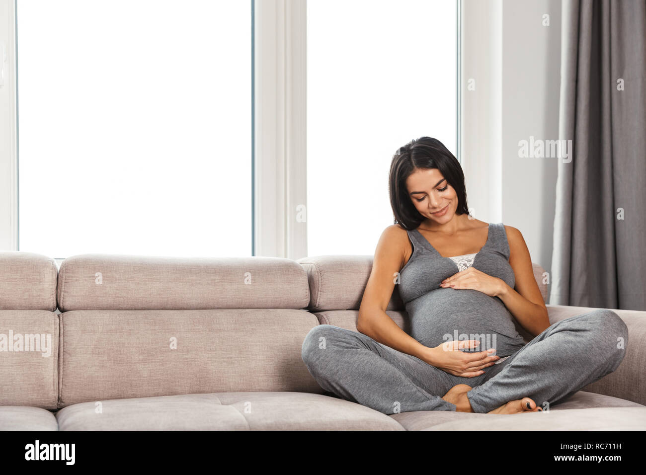 Immagine di un sano incredibile donna incinta al chiuso in casa seduto in posa sul divano. Foto Stock